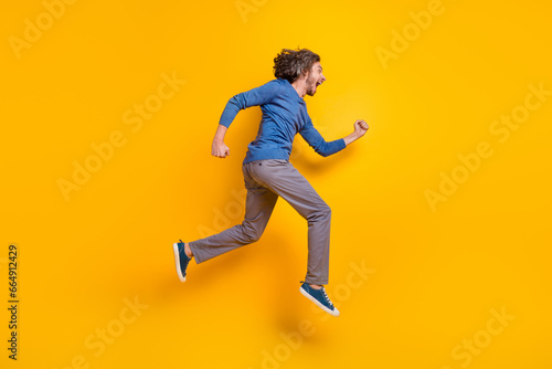 Full length photo of impressed funky guy dressed blue pullover hurrying running jumping high isolated yellow color background