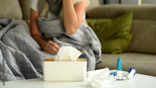 woman is sitting on the sofa, blowing her nose and throwing a crumpled napkin on the table.