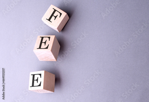 Word FEE on wooden block on the grey background
