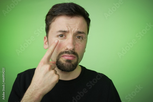 Man gesturing towards his eye, set against a vibrant green background