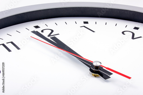 Midnight is coming. Black and white office clock with a red pointer on a gray background.