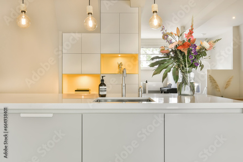 a white kitchen with flowers in the center and light bulbs on the wall above it that are hanging over the sink