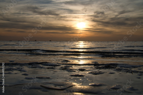 Sunset, small rock at low tide in front of the illuminated sea. Baltic Sea.