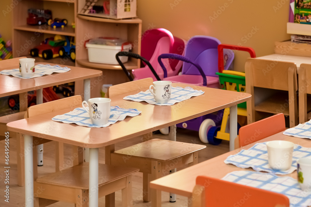 Lunch in kindergarten, on a small table are plates. Meal time in kindergarten. Dining room the wooden chairs and small tables Lunch in kindergarten, on a small table are plates. Meal time in kindergarten. Dining room the wooden chairs and small tables