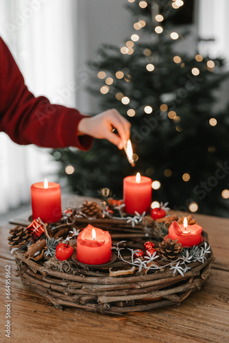 Female hand lighting all four candles on advent wreath on Christmas Eve. Celebrating cozy winter time at home.