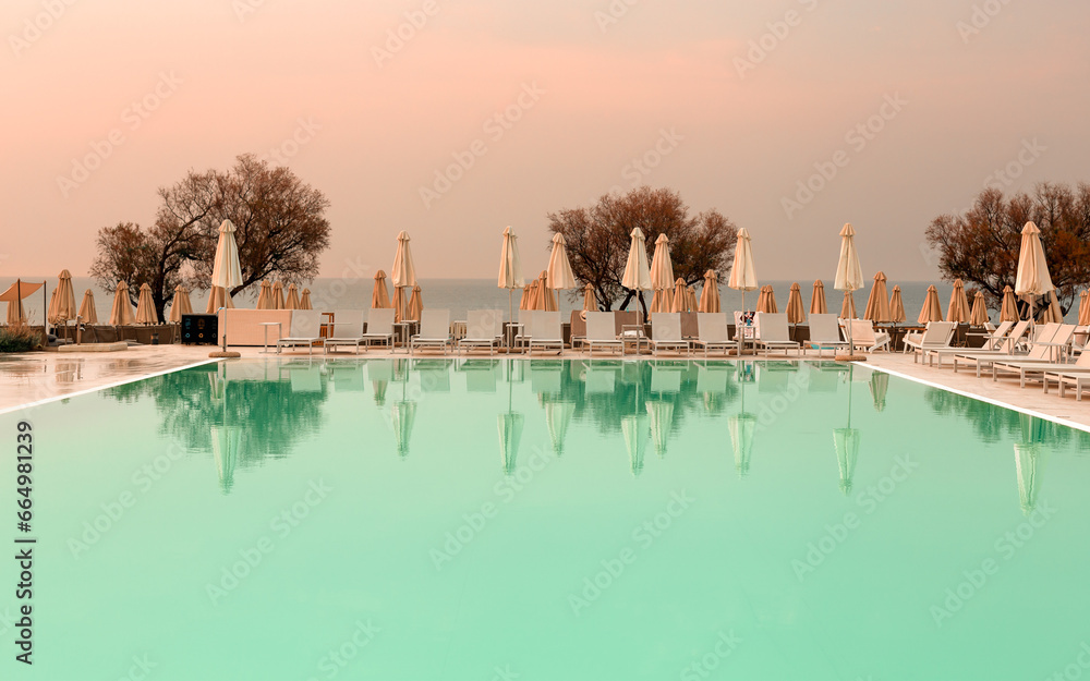 Fototapeta premium Outdoor luxury sunset over swimming pool summer beachfront hotel resort, tropical landscape. Beautiful tranquil beach holiday vacation background. Amazing island sunset beach view, palm trees