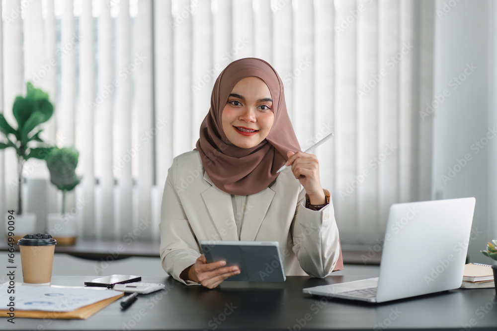 Asian Muslim businesswoman smiling at camera while using tablet. Asian Muslim businesswoman smiling at camera while using tablet.