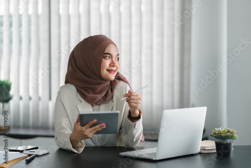 Asian Muslim businesswoman smiling at camera while using tablet.