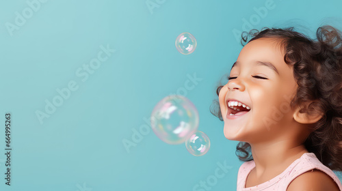 Close-up of a cheerful happy child blowing soap bubbles on a flat color background with copy space. Kindergarten and children activities banner template.