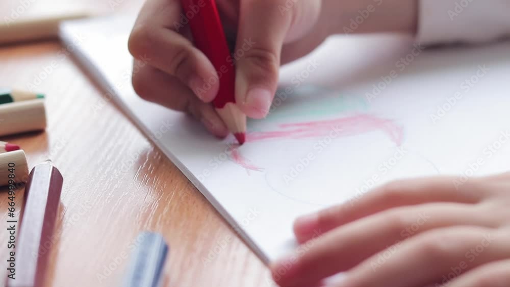 A preschool child draws with colored pencils in an album. Child's hand with a pencil close-up, selective focus. The girl draws a colored cloud A preschool child draws with colored pencils in an album. Child's hand with a pencil close-up, selective focus. The girl draws a colored cloud