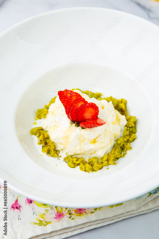 curd dessert with strawberries on top in a white plate on a marble background, side view curd dessert with strawberries on top in a white plate on a marble background, side view