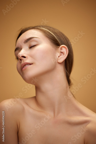 Tenderness. Attractive young girt standing with bare shoulders, health, smooth, spotless skin isolated over light brown background. Concept of natural beauty, skincare, cosmetics and cosmetology