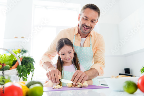 Photo of dreamy positive dad small daughter chopping knife mushrooms preparing supper together indoors home kitchen