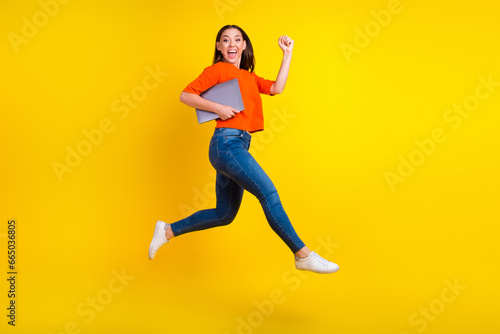 Full body photo of stylish trendy girl jump hold laptop isolated on yellow color background © Tetiana