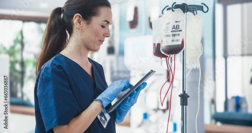 Female Nurse Holding Tablet Computer And Checking The Blood Bag In Donation Center. Professional Caucasian Woman Observing Donation Process In Bright Hospital. Healthcare And Charity Concept. photo