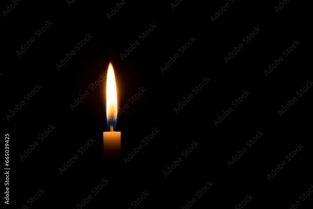 A single burning candle flame or light glowing on an orange candle on black or dark background on table in church for Christmas, funeral or memorial service with copy space A single burning candle flame or light glowing on an orange candle on black or dark background on table in church for Christmas, funeral or memorial service with copy space