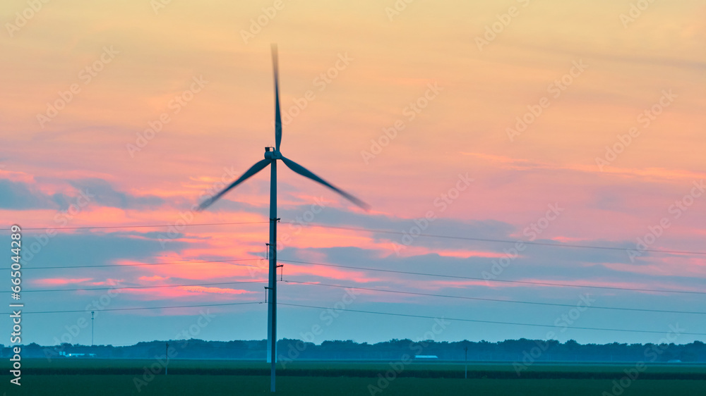 Aerial spinning wind turbine at dusk with pink and blue clouds