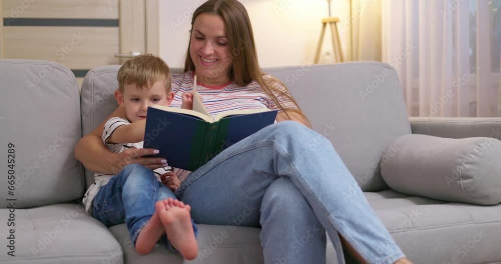 Mother and son are reading a book sitting on a cozy sofa in the living room Mother and son are reading a book sitting on a cozy sofa in the living room