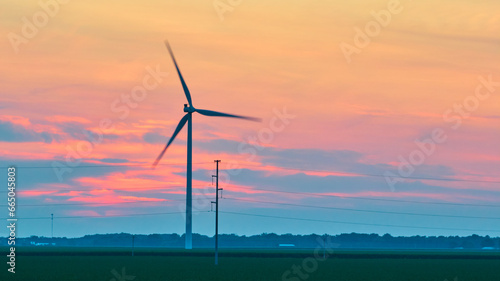 Gorgeous pink and blue sunset clouds behind spinning wind turbine in green field