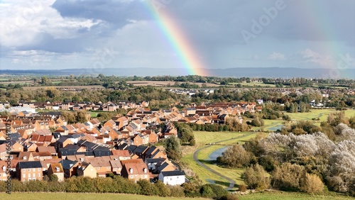 Idyllic landscape of a village situated along a river with a vivid rainbow arching overhead.