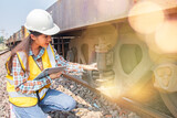 Female railway technician engineer wearing hardhat and vest does field work inspecting bogies underbody device that supports the weight train carriages responsibly controls sway of the train wheels.