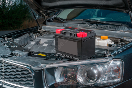 A new battery sits on the engine of a car with the hood open