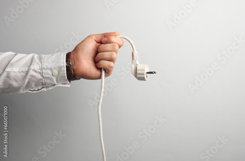 Foto Man's hand in white shirt holds electrical plug on gray background