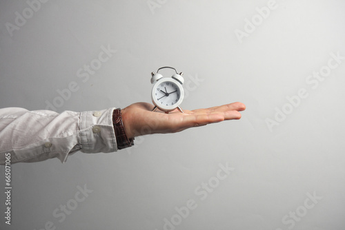 Man's hand in white shirt holds alarm clock on gray background