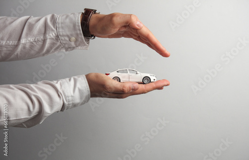 Man's hand in white shirt holds toy car on gray background. Auto insurance
