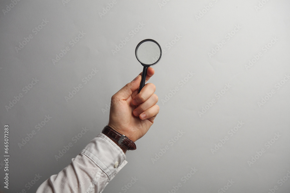 Man's hand in white shirt holds magnifying glass on gray background Man's hand in white shirt holds magnifying glass on gray background