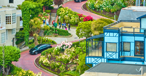 Aerial close up black car driving down Lombard Street with balcony view from blue house