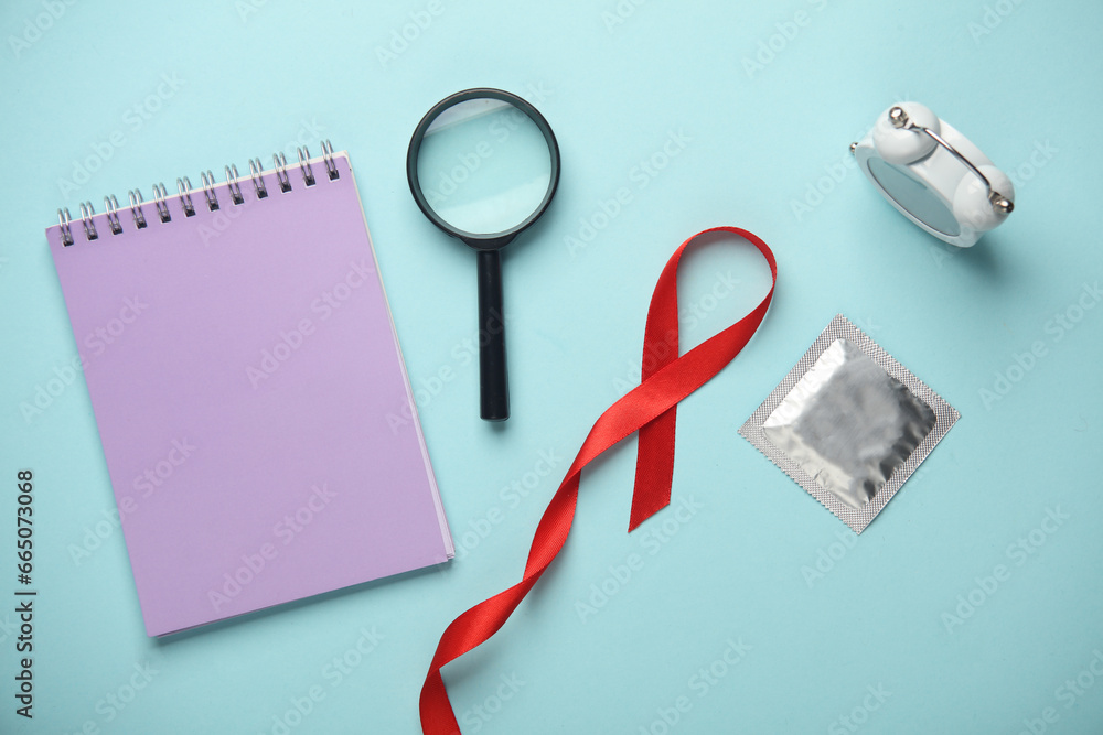 Red AIDS Awareness Ribbon and magnifying glass, condom, notebook on blue Background Red AIDS Awareness Ribbon and magnifying glass, condom, notebook on blue Background