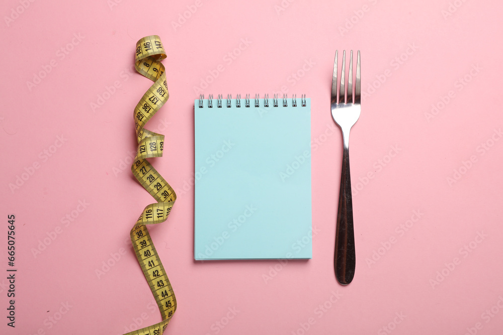 Fork with measuring tape and notebook on pink background. Weight loss, diet concept - obrazy, fototapety, plakaty 