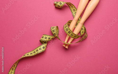 Doll leggs with measuring tape on pink background. Weight loss, diet concept