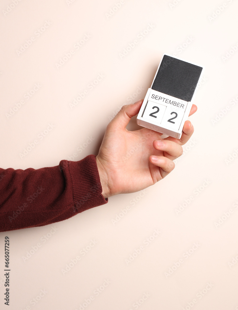 Man's hand in sweater holds block calendar with the date september 22 on a beige background Man's hand in sweater holds block calendar with the date september 22 on a beige background