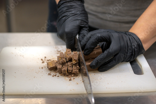 chef cutting sweet chocolate bars with caramel filling , fudge candy for cheesecake preparation photo