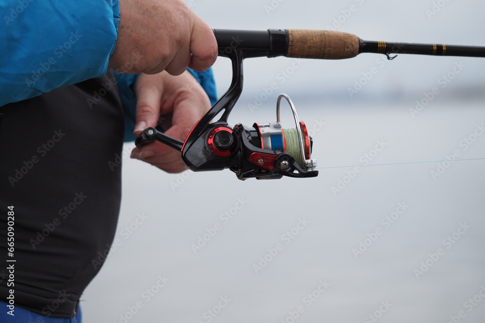 Fishing. A fishing rod with a reel in the hands of a fisherman. Close-up.