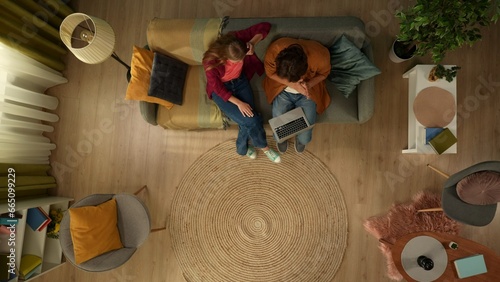 Top view capturing a young couple sitting on the couch, hugging and talking, looking at the laptop screen as if they are searching for something online. photo