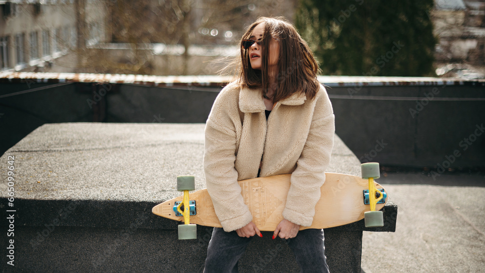 Fototapeta premium Pretty woman sitting with skateboard on sunlight rooftop