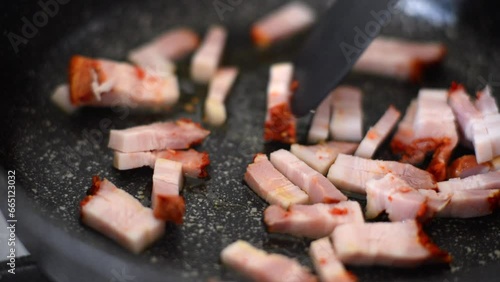 Slices of chopped bacon are fried in oil in a frying pan photo