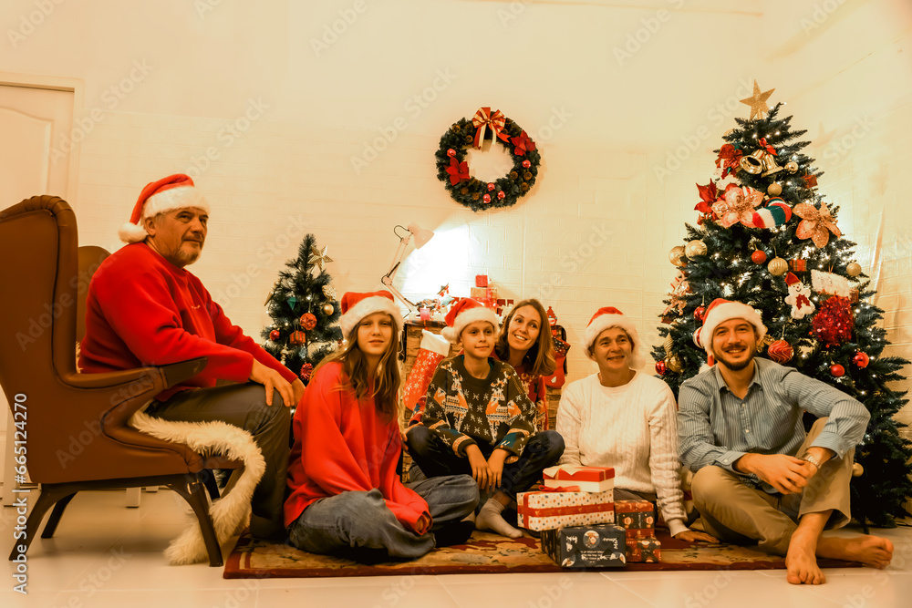 Multi-Generation Family Exchanging And Opening Gifts Around Christmas Tree At Home. Christmas family portrait - family sitting on floor front of beautiful Christmas tree.