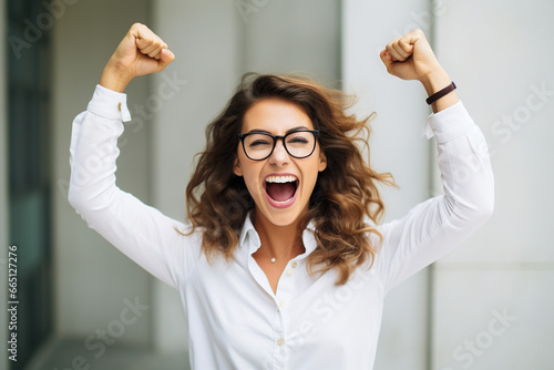 Portrait of overjoyed attractive woman standing with excited expression, raising fists, screaming, shouting yeah, celebrating her victory, success.