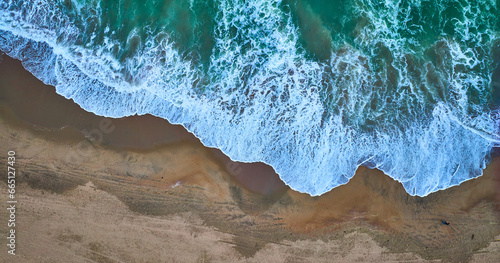 Downward aerial of receding green ocean waves on top with dark tan sandy beach on bottom © Nicholas J. Klein