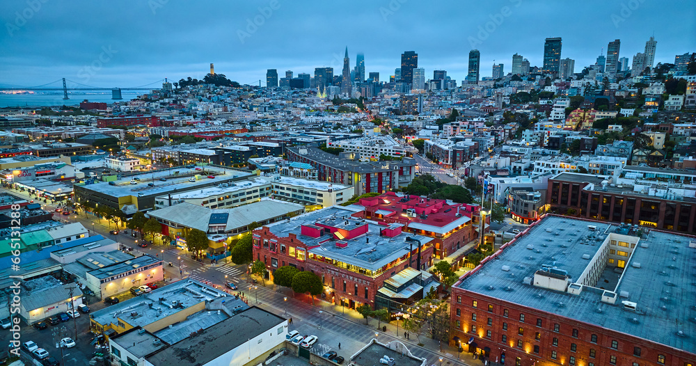 Fishermans Wharf aerial at dusk with lights on in the city and downtown skyscrapers in distance