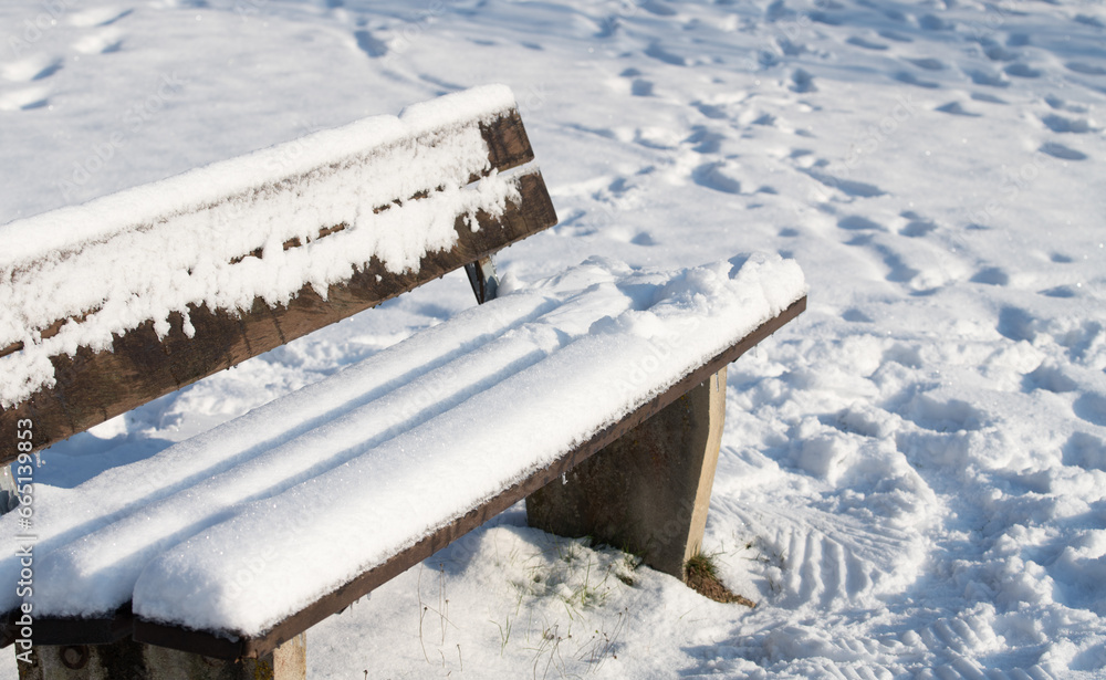 In winter there is a white wooden bench in the middle of the snow. The bench is also covered in snow. There is space for text. In winter there is a white wooden bench in the middle of the snow. The bench is also covered in snow. There is space for text.