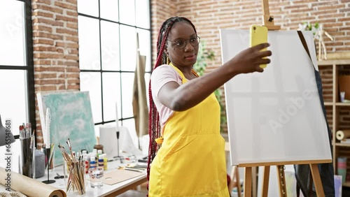 Confident african american woman artist smiling as she boldly makes a selfie with her smartphone at her inspiring art studio photo