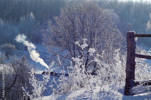 Winter atmosphere in the village, frost on the trees and smoke above the rural house.