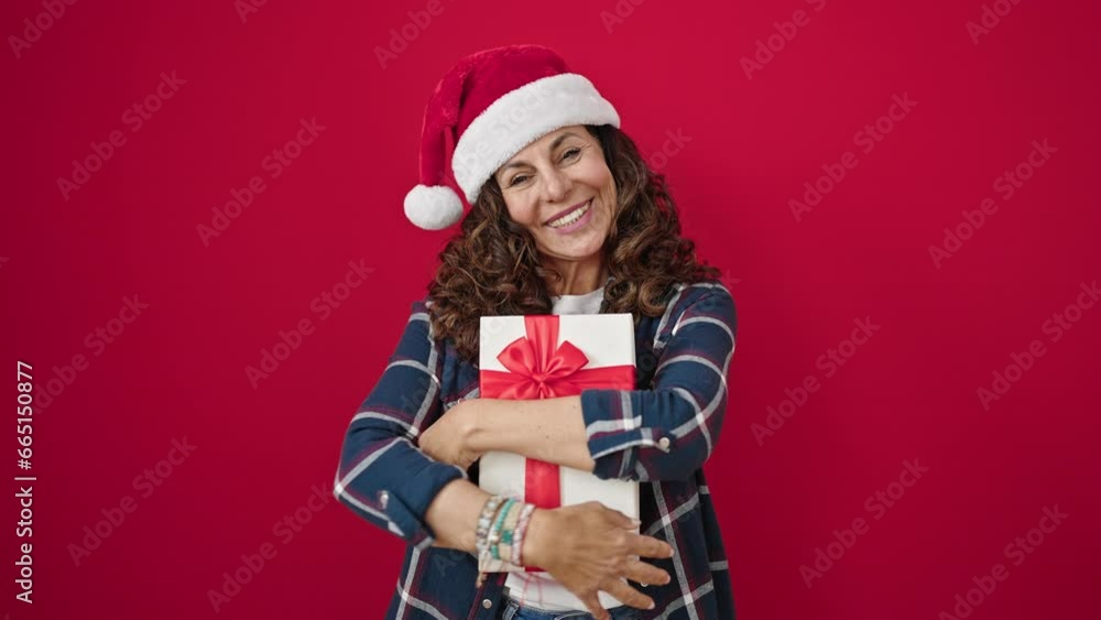 Middle age hispanic woman smiling confident hugging christmas gift over isolated red background Middle age hispanic woman smiling confident hugging christmas gift over isolated red background