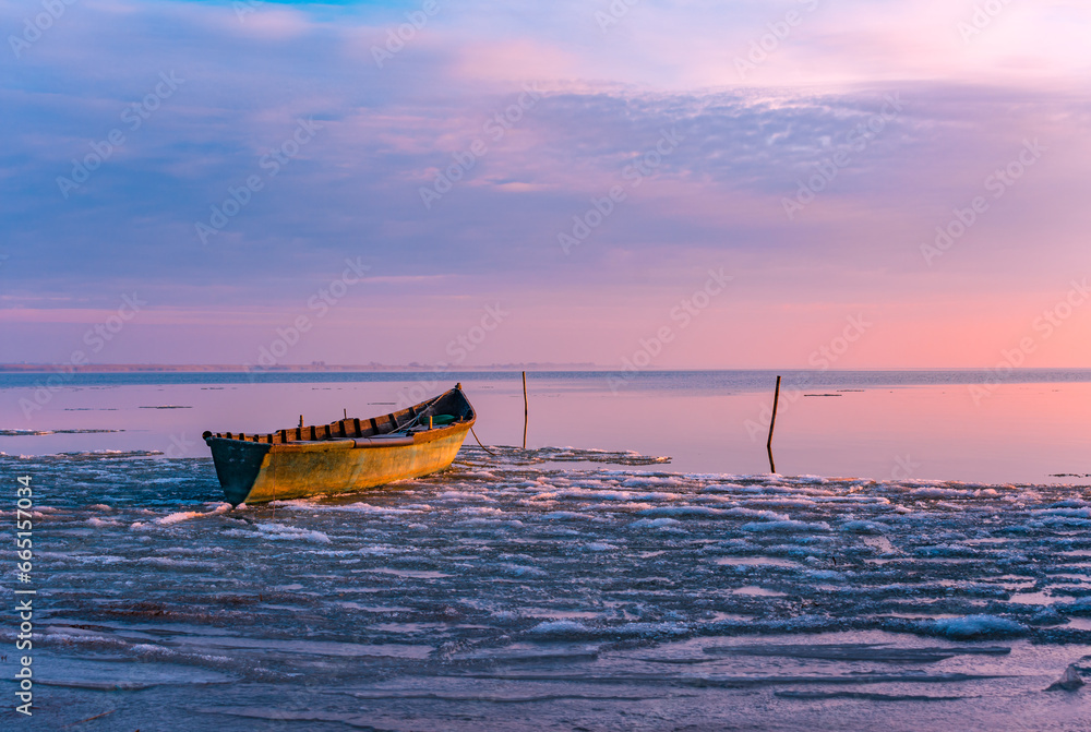 frozen boat in winter on the lake at sunrise