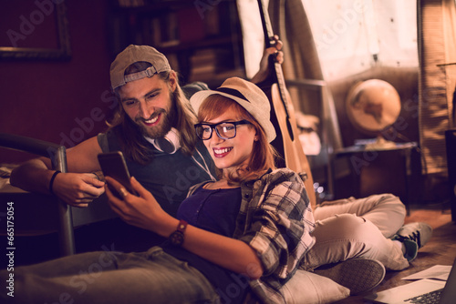 Loving young couple looking at the smartphone while playing guitar in the bedroom
